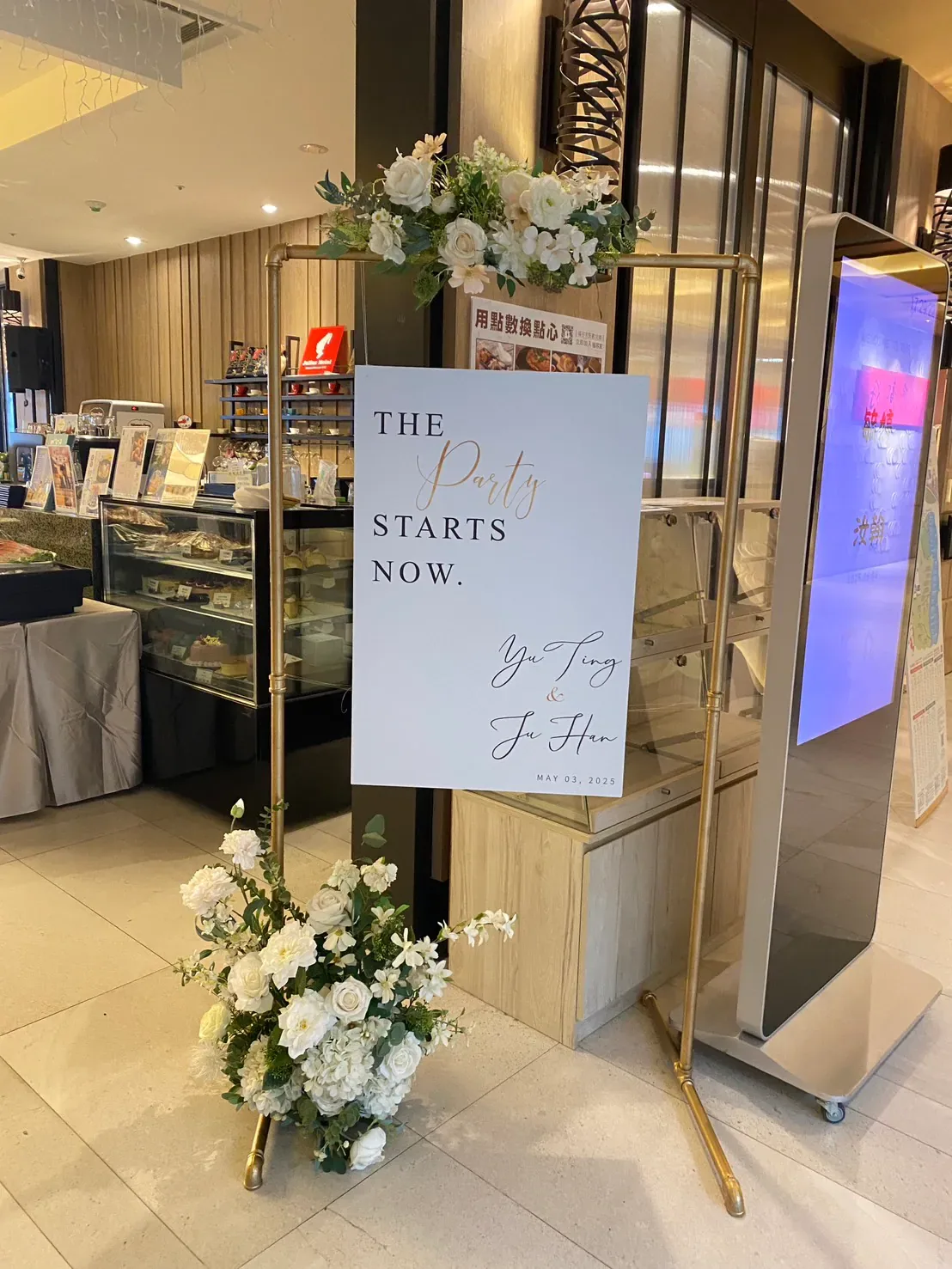 宴會廳內金色鐵架迎賓看板與白色花藝佈置