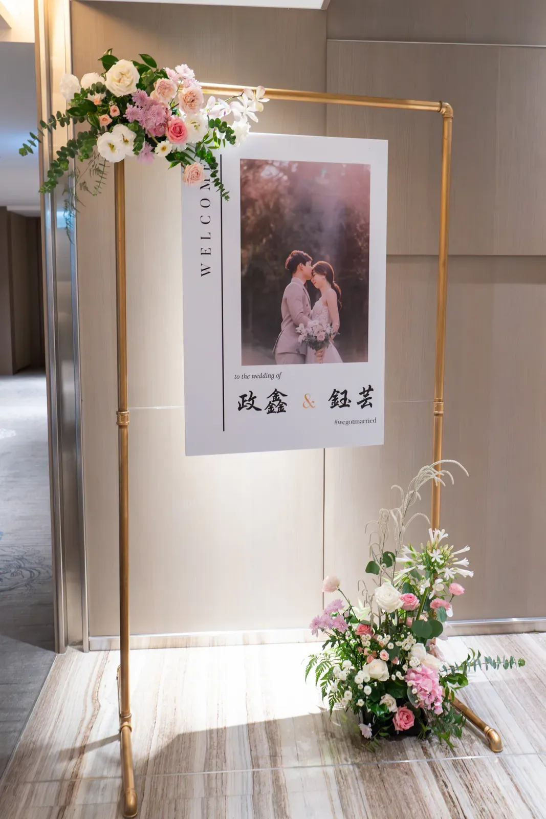 國泰萬怡婚禮室內迎賓立牌，金色鐵架綴粉白鮮花與落地花藝