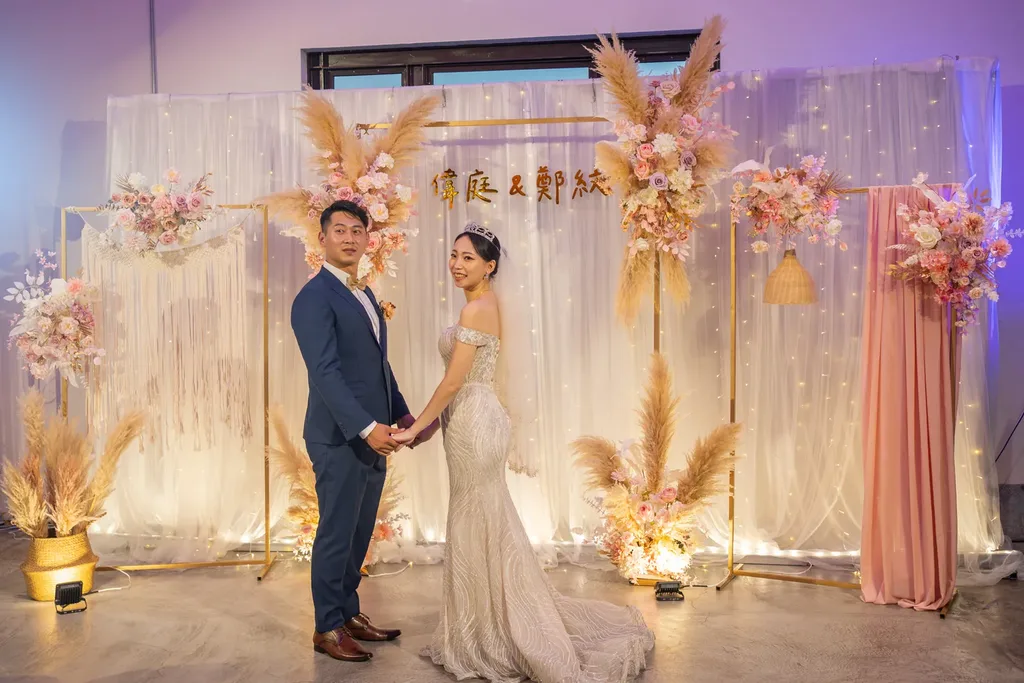 瓶蓋工廠婚禮佈置新人合影，蒲葦燈牆背板前粉色復古工業風場景