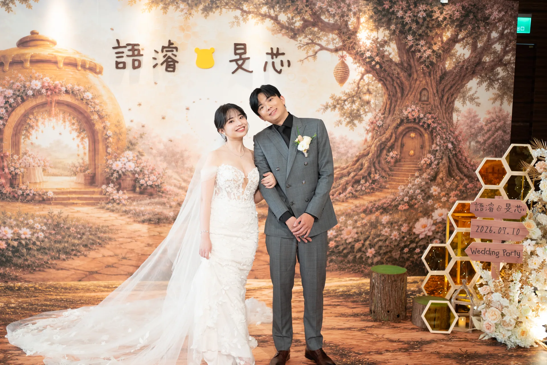 新人在小熊維尼主題婚禮主背板前合照,大直典華花田盛事廳百畝森林場景、蜂蜜罐與六角蜂巢展示櫃