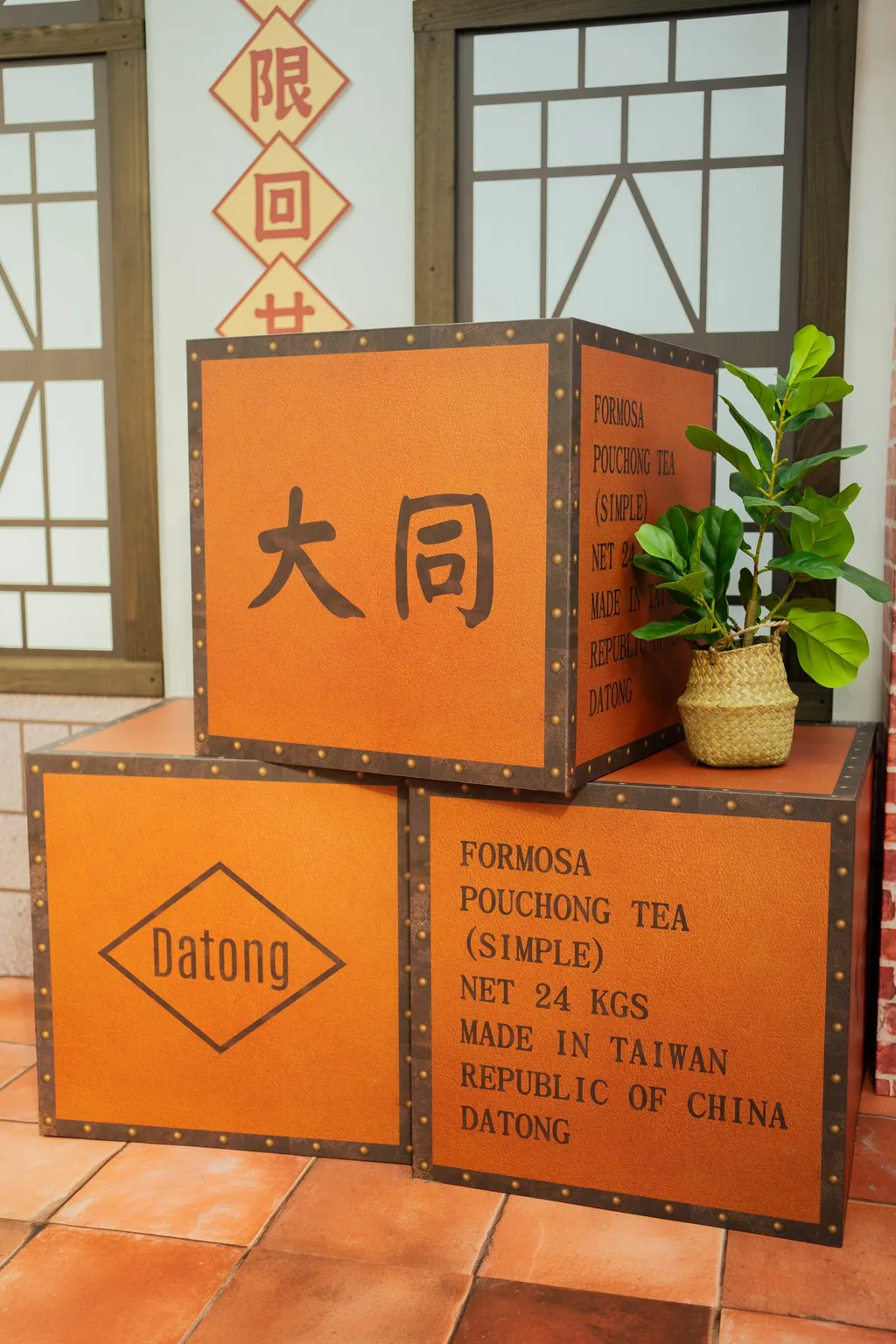 大同戶政背板的茶箱道具細節,仿老茶箱鉚釘包邊做出量體:一面手寫「大同」,一面菱形框寫 Datong,一面整面印 FORMOSA POUCHONG TEA (SIMPLE)/NET 24 KGS/MADE IN TAIWAN/REPUBLIC OF CHINA/DATONG。
