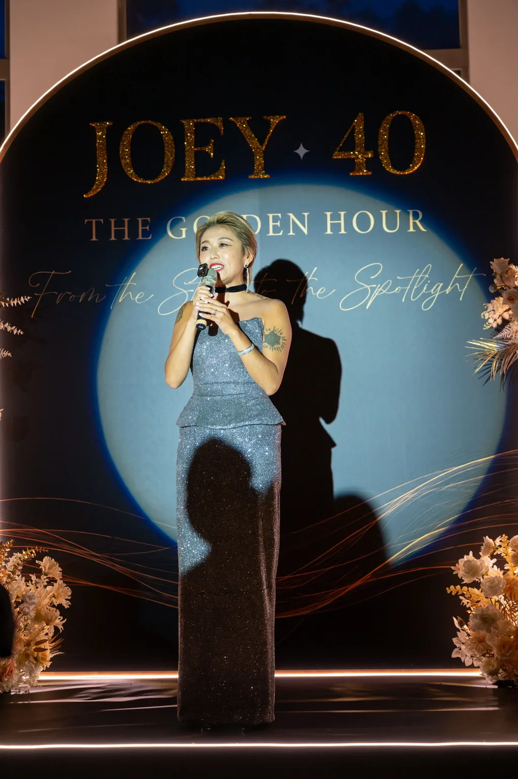 Joey 在舞台上舉杯致詞，背後是 JOEY 40 The Golden Hour 背板