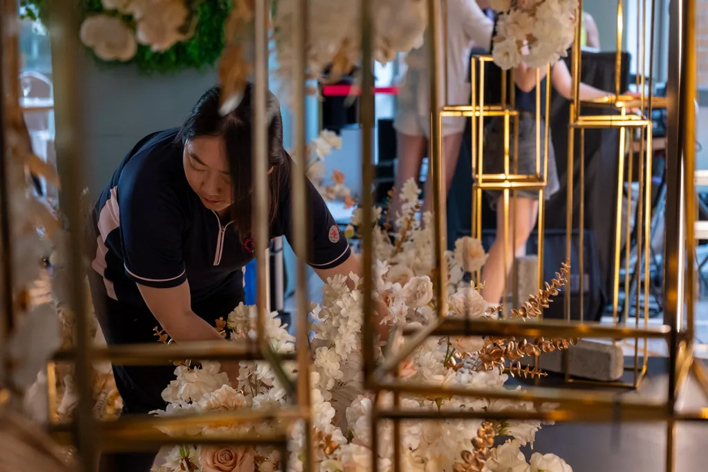 舞台兩側的花藝，米白香檳色花材架在金色框架上，進場時整理中
