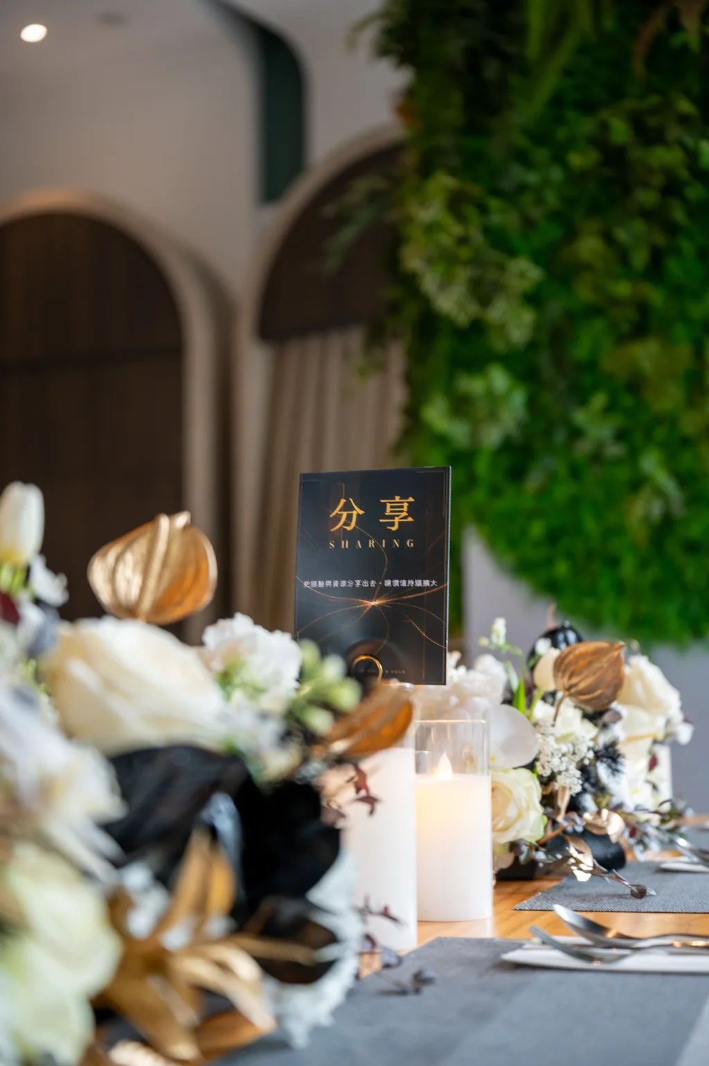 桌名立牌「分享」與桌花特寫，白花、金色火鶴與黑葉，前面一盞仿真蠟燭