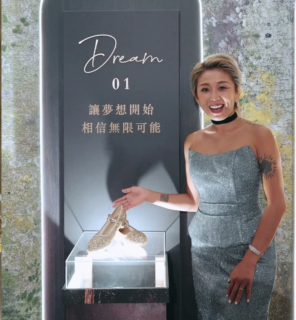 壽星站在光的軌跡 01 Dream 看台旁伸手指向展示罩,看台上寫著「讓夢想開始 相信無限可能」,背景是弧形花牆