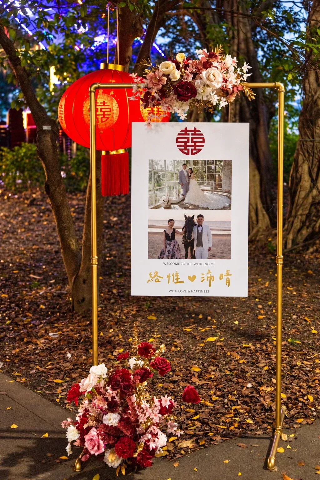 夜裡的金色框架迎賓牌,框頂與地面有酒紅與米白花藝