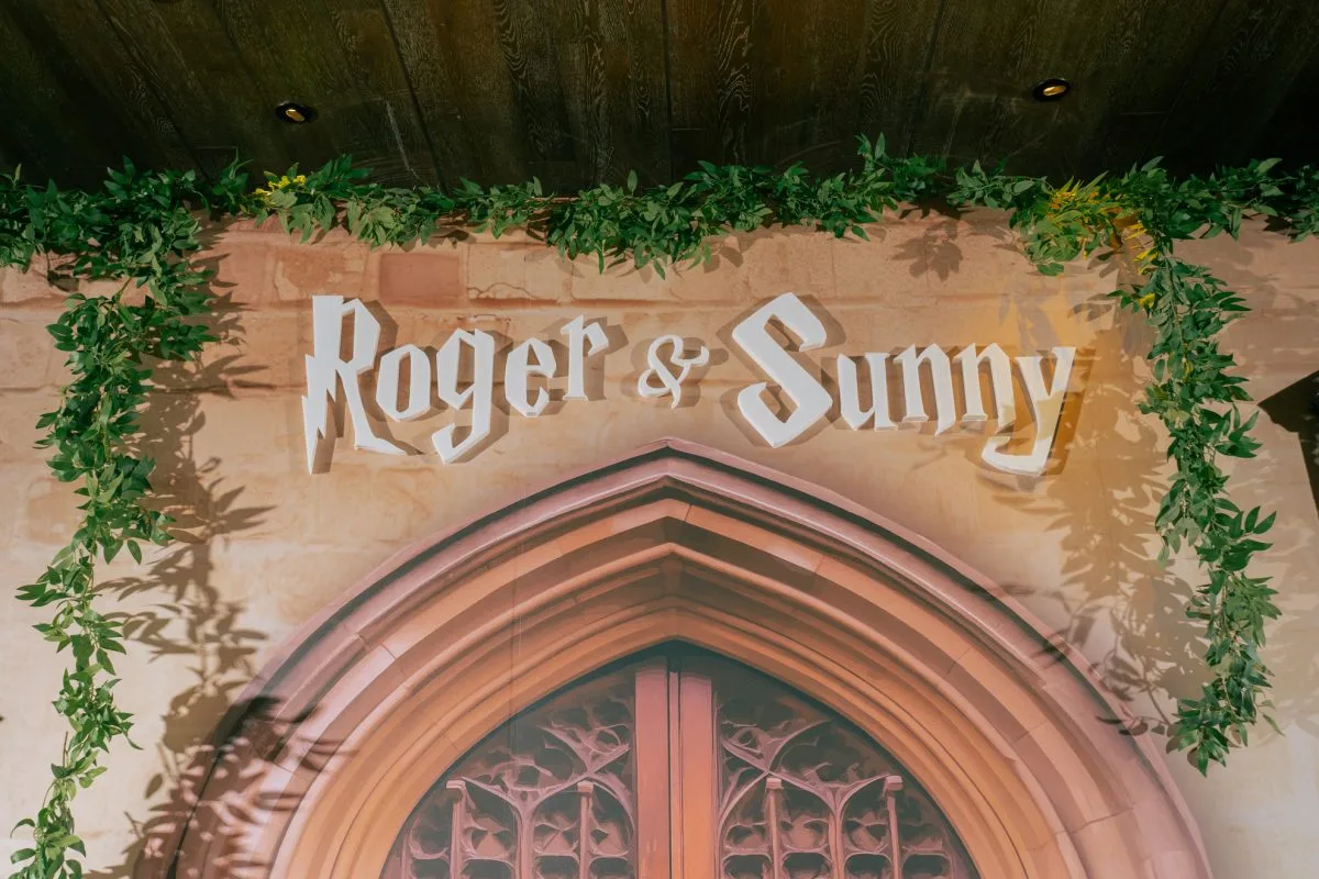 以磚牆與哥德式拱門為背景，點綴綠藤，白色「Roger & Sunny」字樣為婚禮增添浪漫。