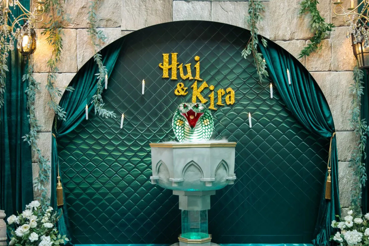 Hui & Kira婚禮佈景，墨綠絲絨拱門，金色姓名，蛇形噴泉，燭光點翠綠絲絨背景，金字「Hui & Kira」，蛇頭雕塑、蠟燭與白花，神秘婚禮佈置。