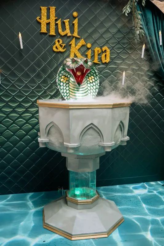 金色Hui & Kira標誌，綠色背景襯托，吐霧眼鏡蛇雕塑與燭台，神秘主題婚禮佈置。