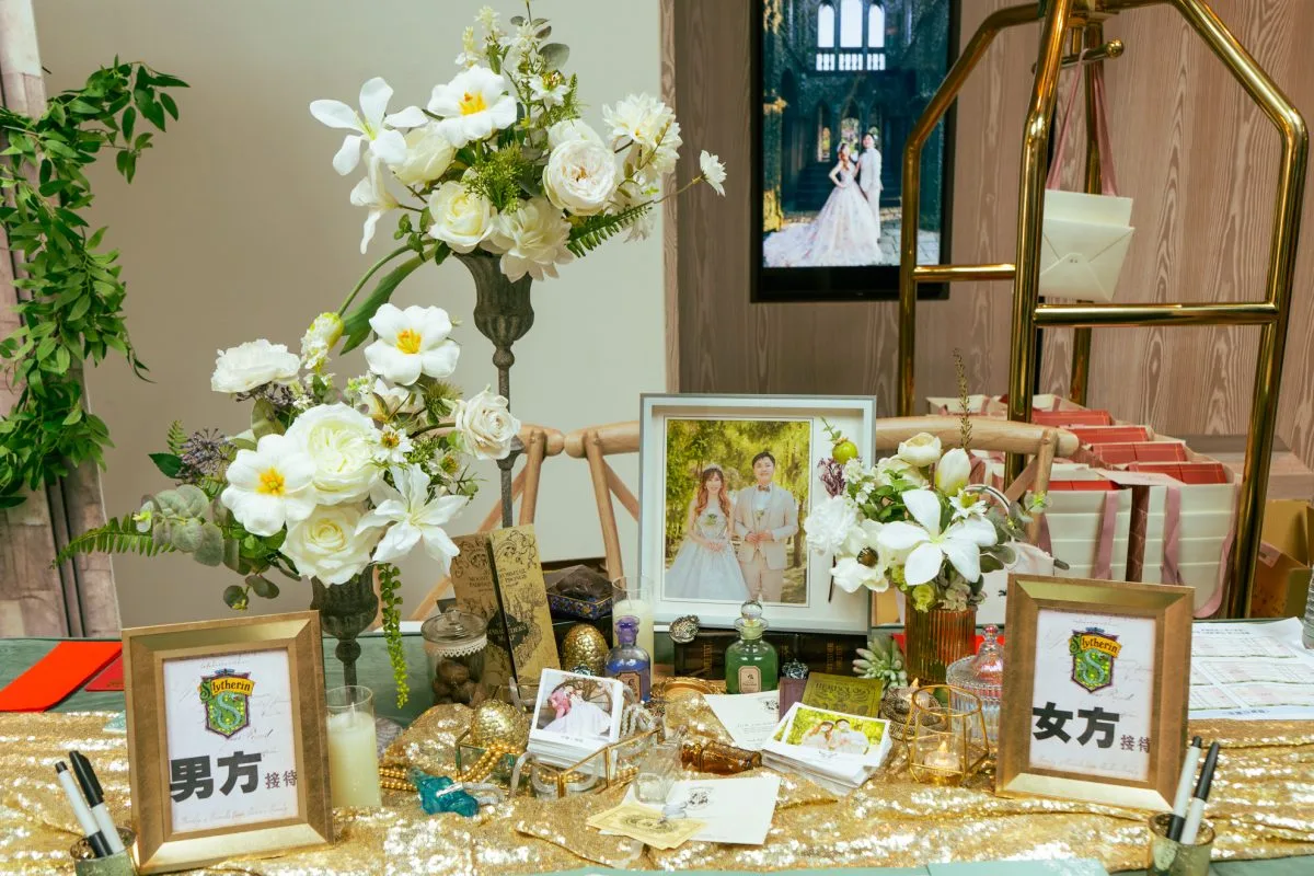 典雅婚禮接待桌，白花綠葉與新人合照，金色佈置，點綴哈利波特元素。