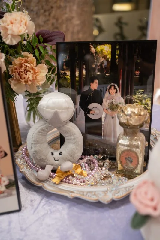 婚禮相框、鑽戒玩偶與飾品擺件,暖色調的花藝點綴著浪漫氛圍。