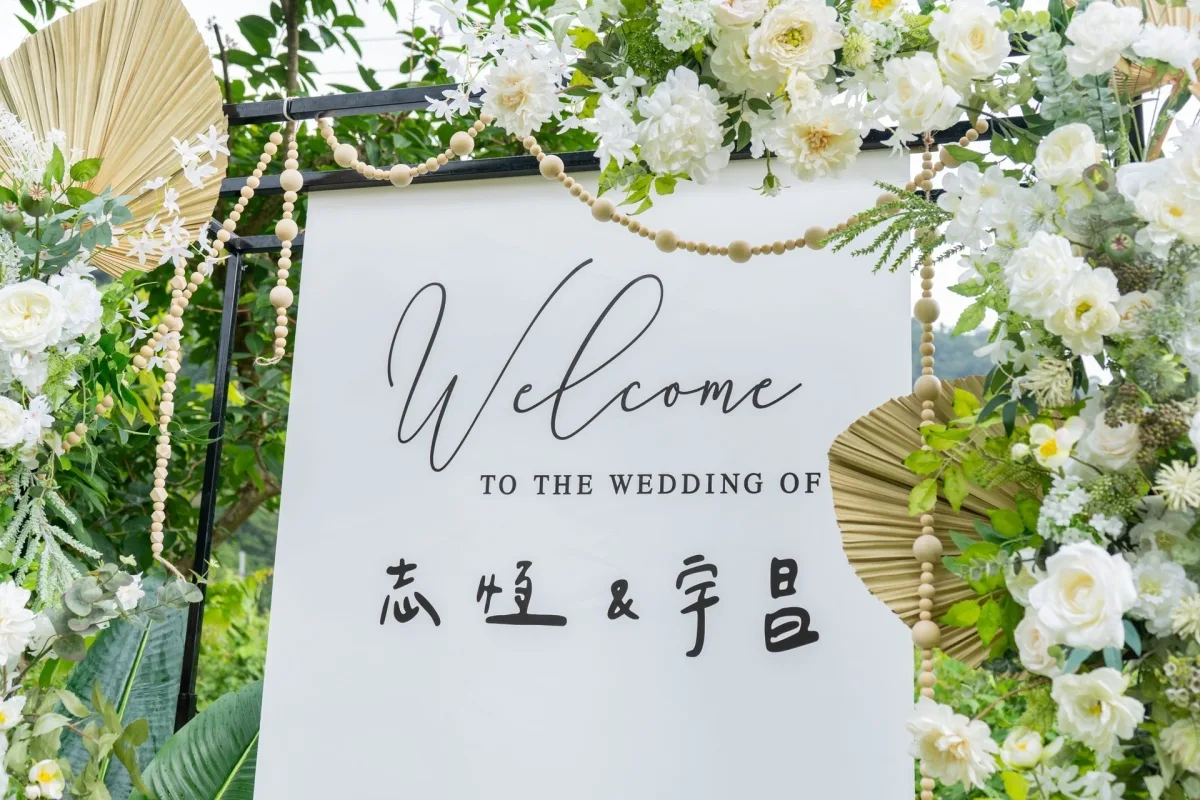 婚禮歡迎牌,周圍環繞白色鮮花與綠葉,木珠點綴,營造自然清新氛圍。