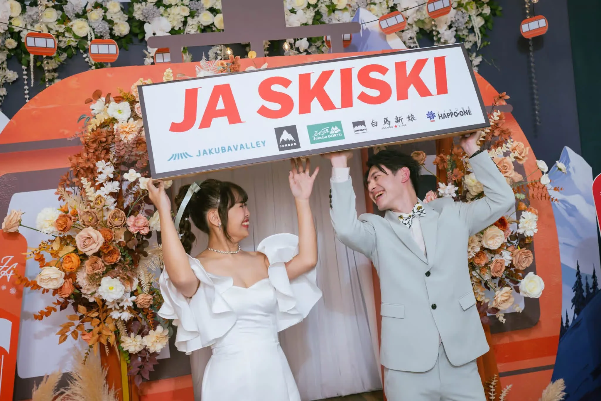 溫馨婚禮，新人於秋意花藝與滑雪纜車背景前，手舉「JA SKISKI」招牌。