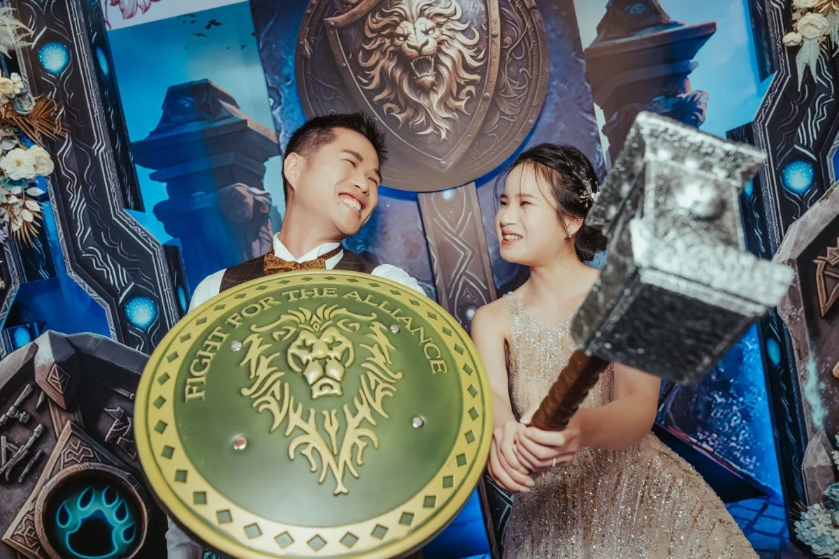 新婚夫婦於魔獸世界主題背景前,手持聯盟盾與戰鎚,面帶幸福笑容。