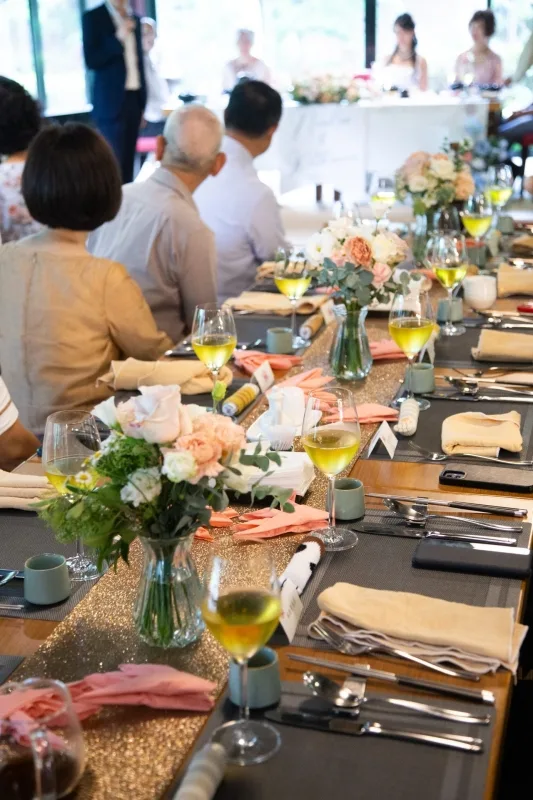 婚宴桌上，金色桌旗、粉白花束和酒杯，暖色調營造浪漫溫馨氛圍。