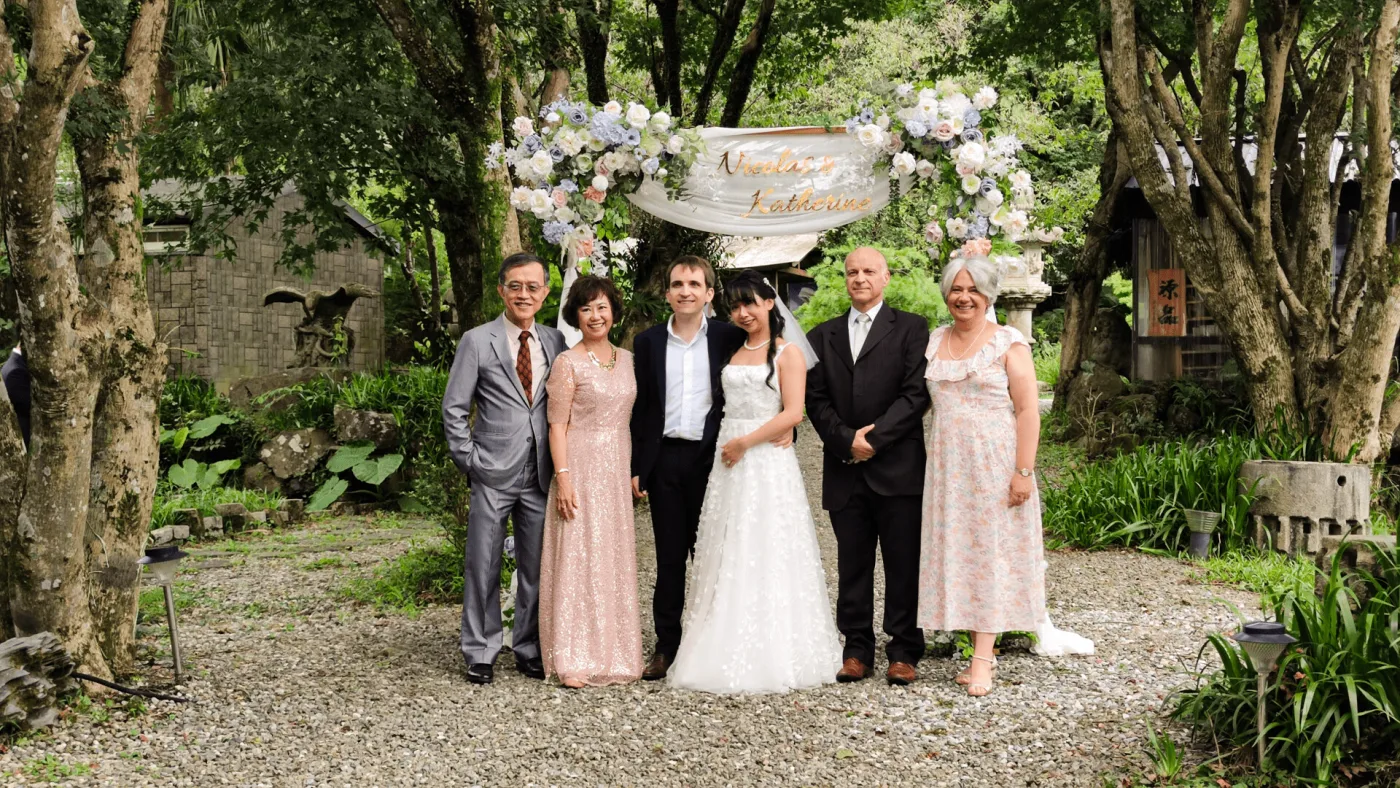 綠意盎然的戶外婚禮，新婚夫婦與親友於花拱門下合影，色調溫馨。