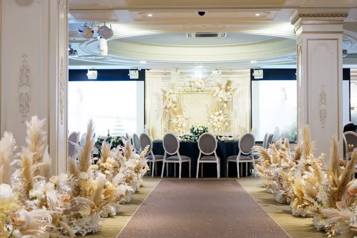 華麗婚宴會場，典雅米白色調，走道兩側飾以蘆葦與花藝，金色背景溫馨浪漫。