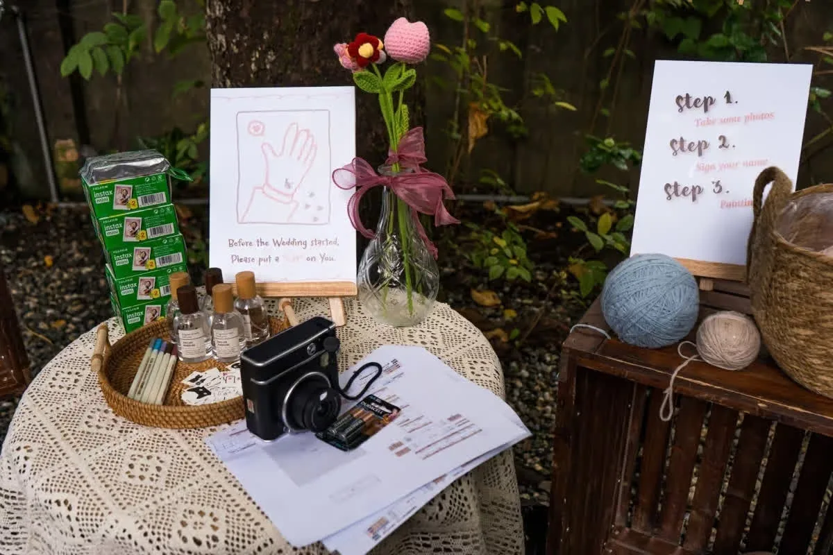 婚禮迎賓區，拍立得、針織花束與簽名指引，溫馨自然色調中洋溢喜慶。