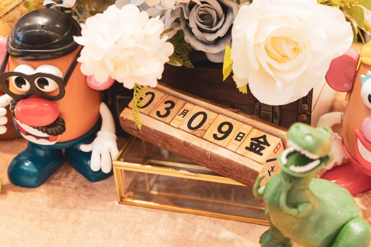 婚禮佈景,有馬鈴薯頭先生、恐龍玩具、柔和色調花藝及木質日期牌。