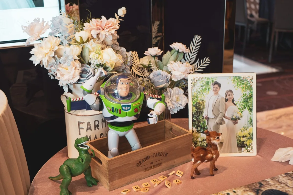婚禮桌上,巴斯光年、恐龍、小鹿伴隨婚紗照與粉藍花藝,氛圍浪漫溫馨。