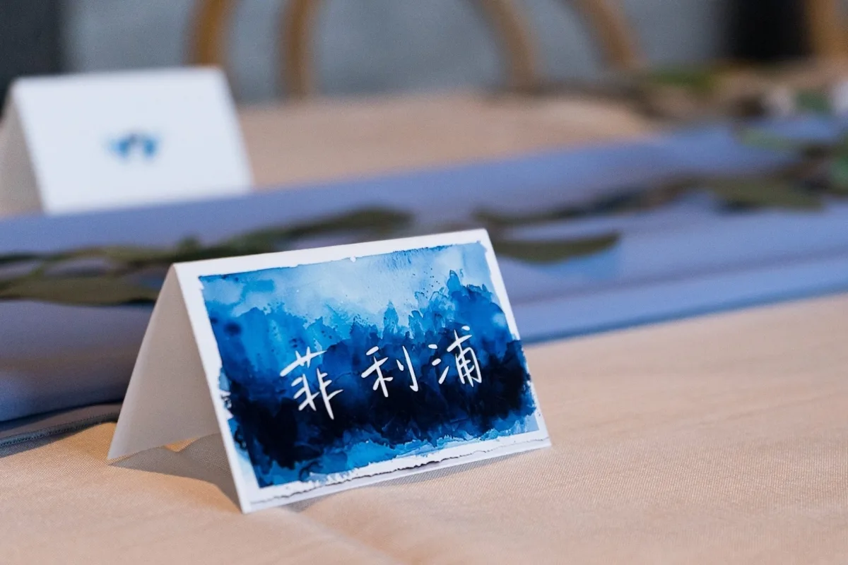 藍色水彩婚禮名牌，淺色桌布搭配藍色桌旗與綠植，風格優雅。