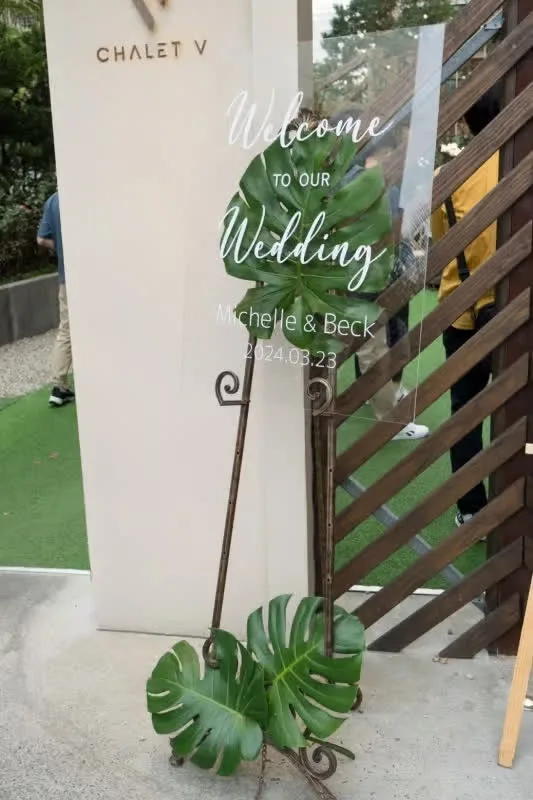 透明壓克力婚禮迎賓牌，飾以綠色龜背芋，棕色支架，營造自然溫馨氣氛。