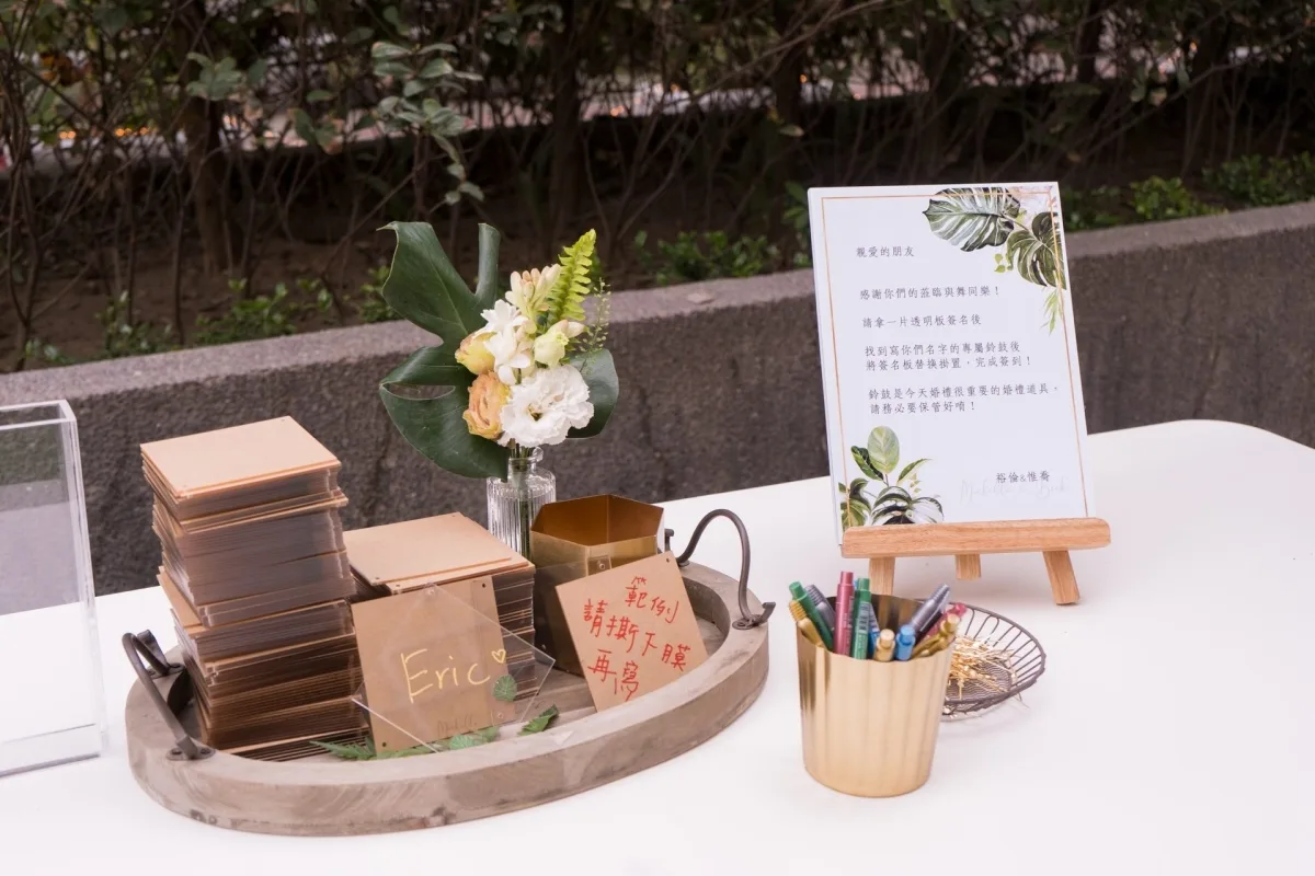 婚禮迎賓桌，擺放簽名板、鮮花與金色筆筒，色調溫暖典雅。