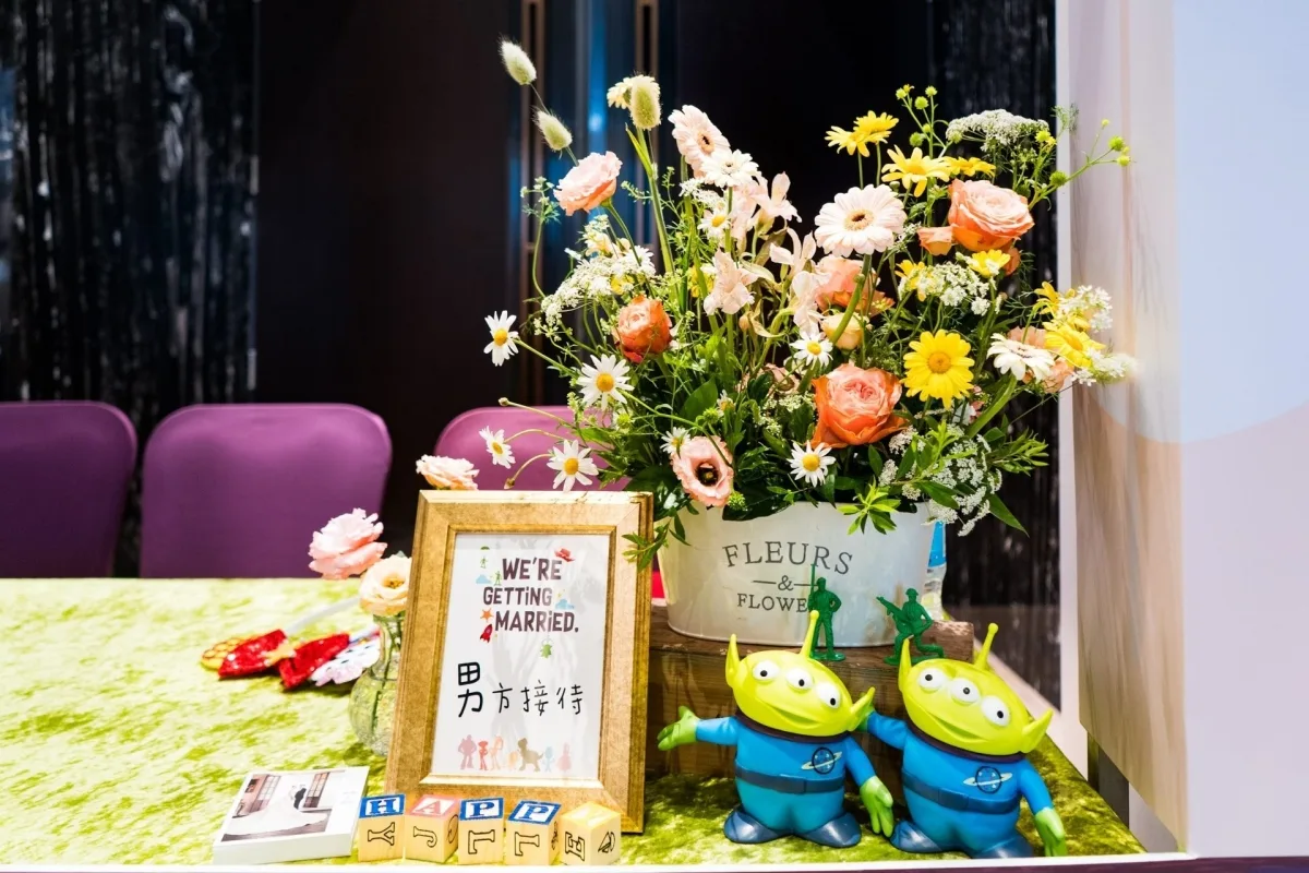 婚禮接待桌，擺放鮮花、結婚標語與玩具總動員外星人，色彩鮮豔溫馨。