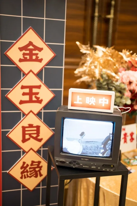 復古電視播映黑白婚禮畫面，金玉良緣對聯，金色系花卉，喜氣洋洋。
