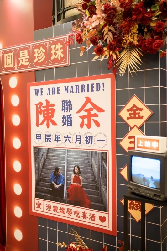 鮮紅花藝點綴藍磚牆，婚禮公告與新人照，復古電視播放喜悅畫面。
