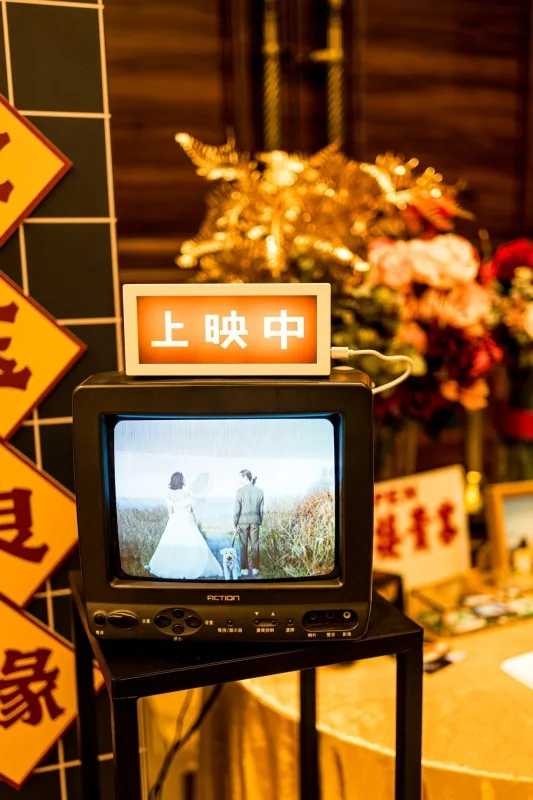 懷舊電視播放婚禮影像，新郎新娘與小狗入鏡，溫暖色調搭配花藝及中式裝飾