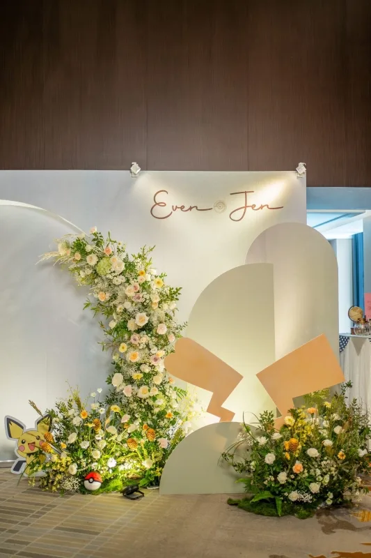 柔和色調婚禮背板，花藝簇擁「Even & Jen」金色簽名，皮卡丘和寶可夢球妝點。