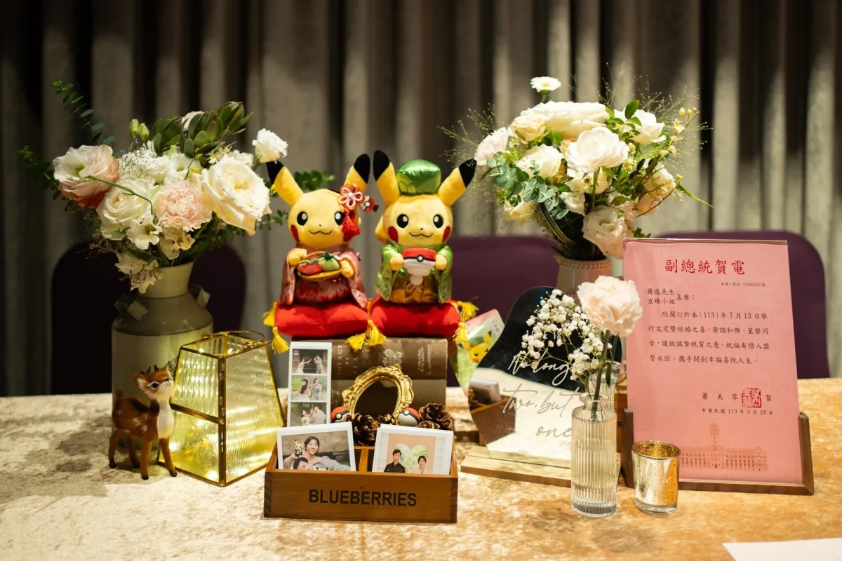 一對穿著傳統服飾的皮卡丘玩偶、溫馨花藝和婚禮照片，色調溫暖。