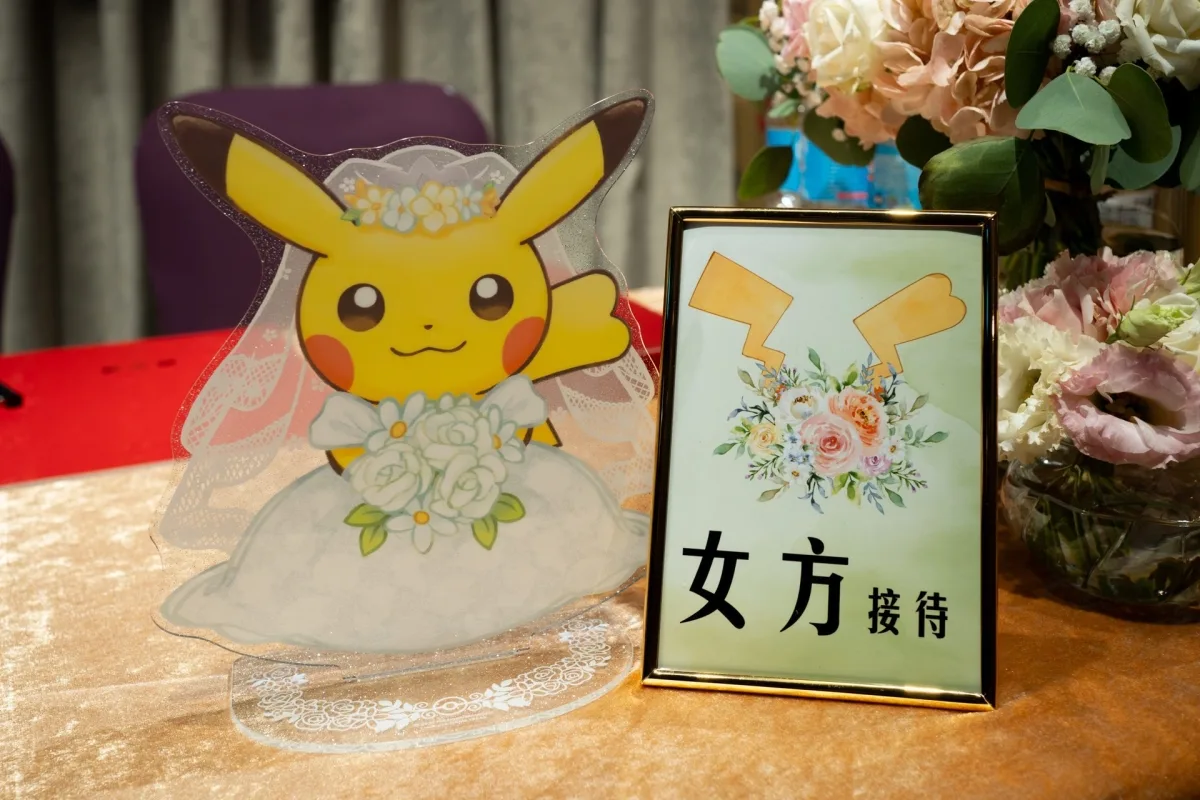 婚禮接待桌上，穿婚紗的皮卡丘公仔與溫馨花卉佈置，色調優雅