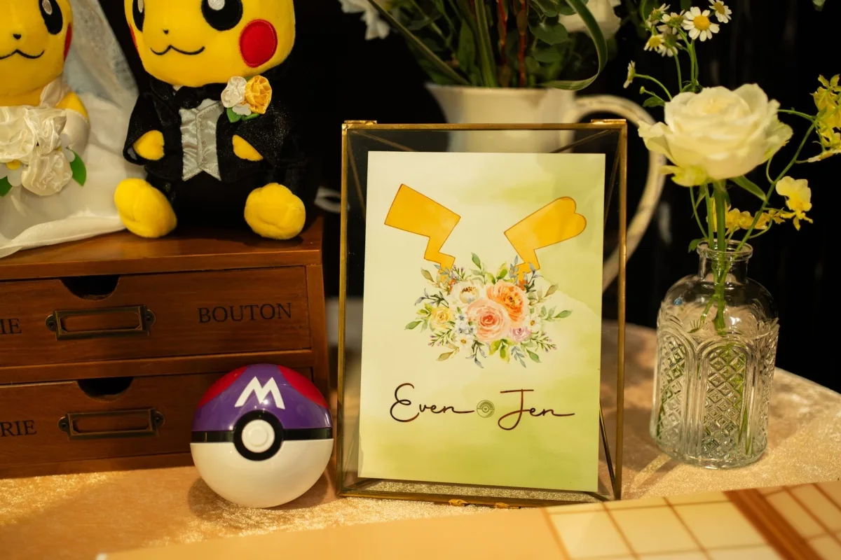 溫馨婚禮佈置，皮卡丘新人玩偶、寶可夢球、花藝名牌，整體暖黃綠色調。