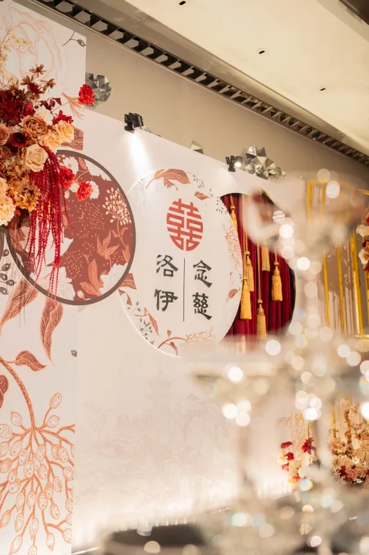 喜慶婚禮佈景,紅橘色花藝與雙喜字,洛伊俞蘊名字,金紅流蘇典雅溫馨。