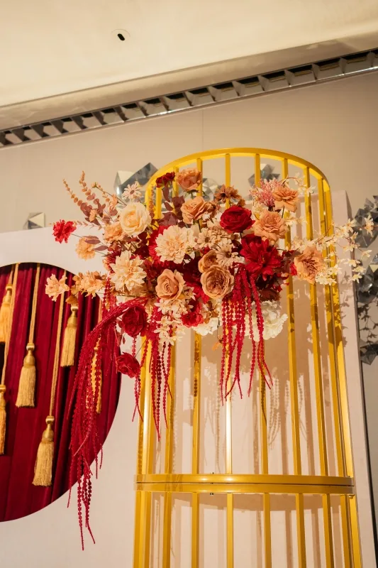華麗金色拱門花藝裝飾,搭配紅絲絨流蘇背景,呈現溫暖喜慶的婚禮氛圍。