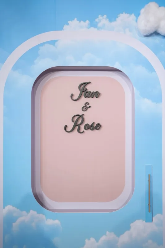 藍天白雲拱門背景，粉色框中Ian與Rose的名字，展現浪漫婚禮氛圍。