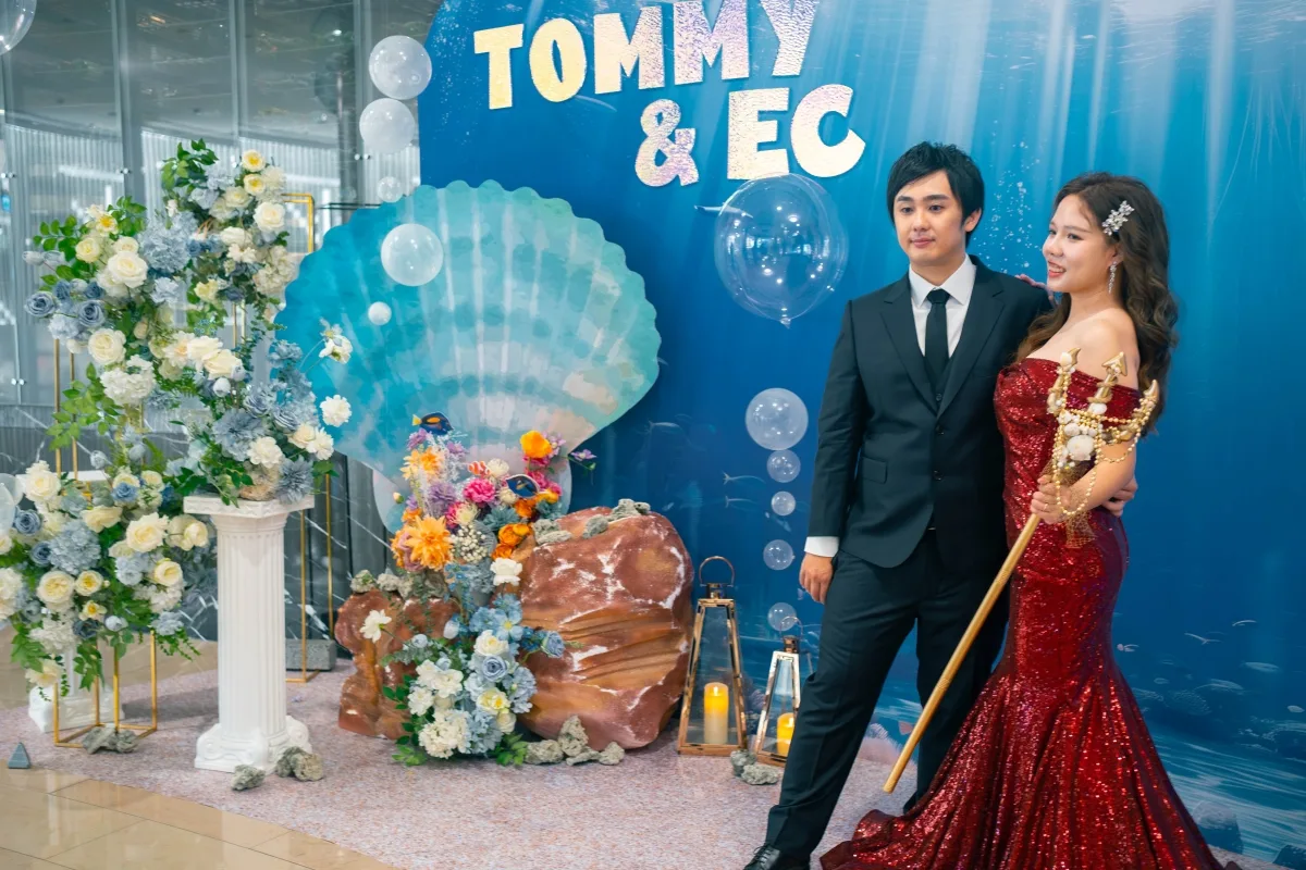 海底主題婚禮中,穿紅禮服的新娘與黑西裝新郎,花卉佈置浪漫溫馨。