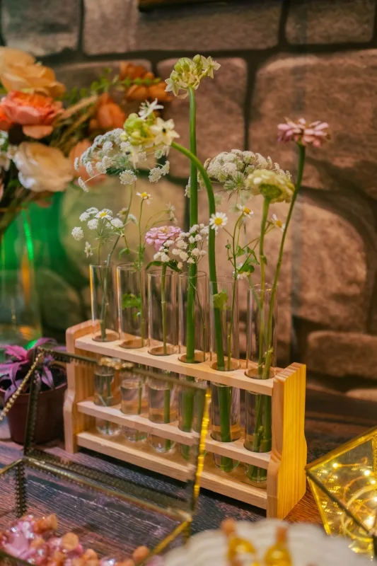 溫馨婚禮裝飾，木架試管中插滿白粉色鮮花，背景是暖色調石牆。