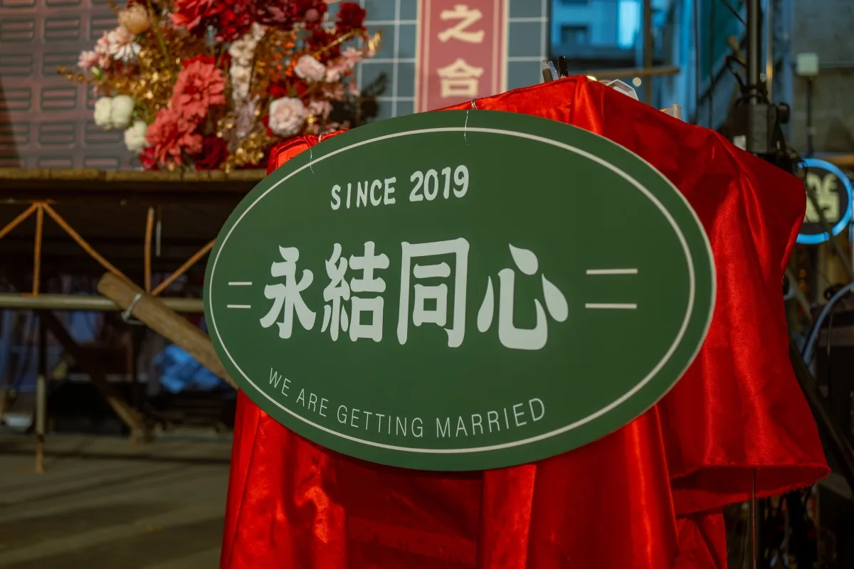 綠色「永結同心」婚禮告示牌，紅花簇擁，喜慶溫馨。