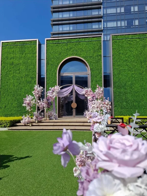 翠綠牆面建築前，紫色花藝裝飾的戶外婚禮場景，氛圍浪漫。