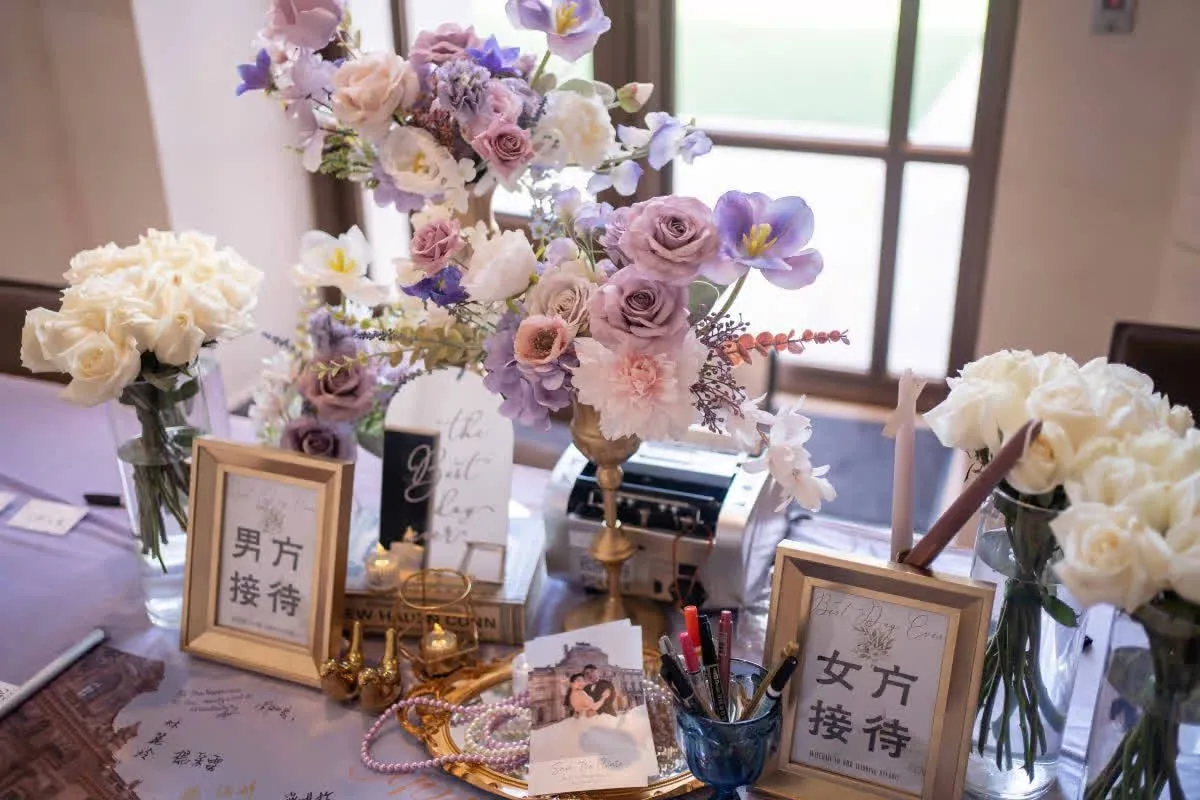 婚禮接待桌佈置，有粉紫白色花藝、金色相框、珍珠飾品，色調溫馨典雅。