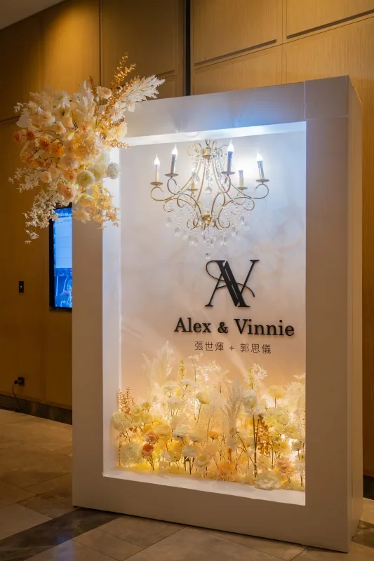 Alex & Vinnie 婚禮迎賓牌，暖色調花藝與水晶吊燈，浪漫優雅。