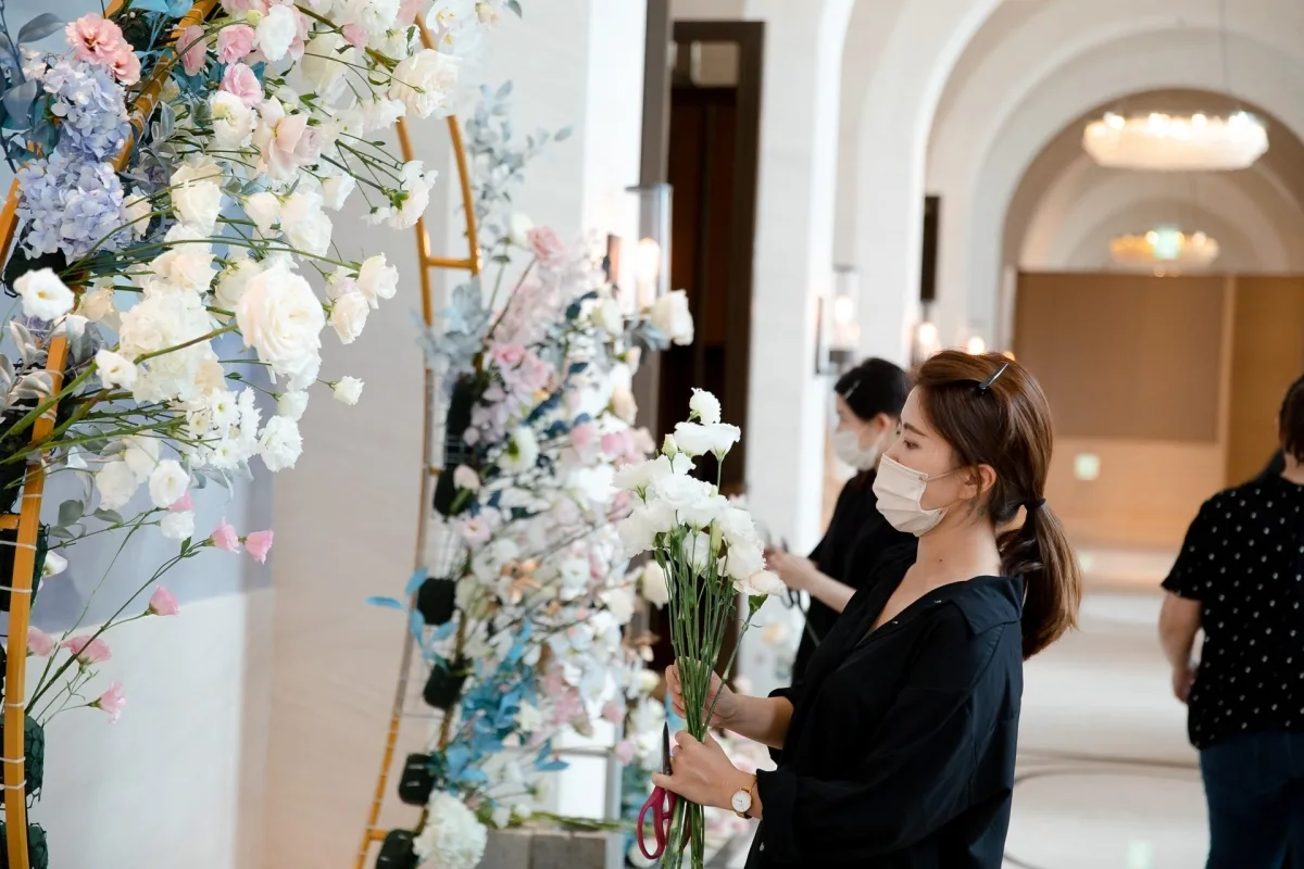 一位女子在婚禮會場佈置花藝拱門，白色、粉色、淺藍色花朵營造優雅浪漫氛圍。