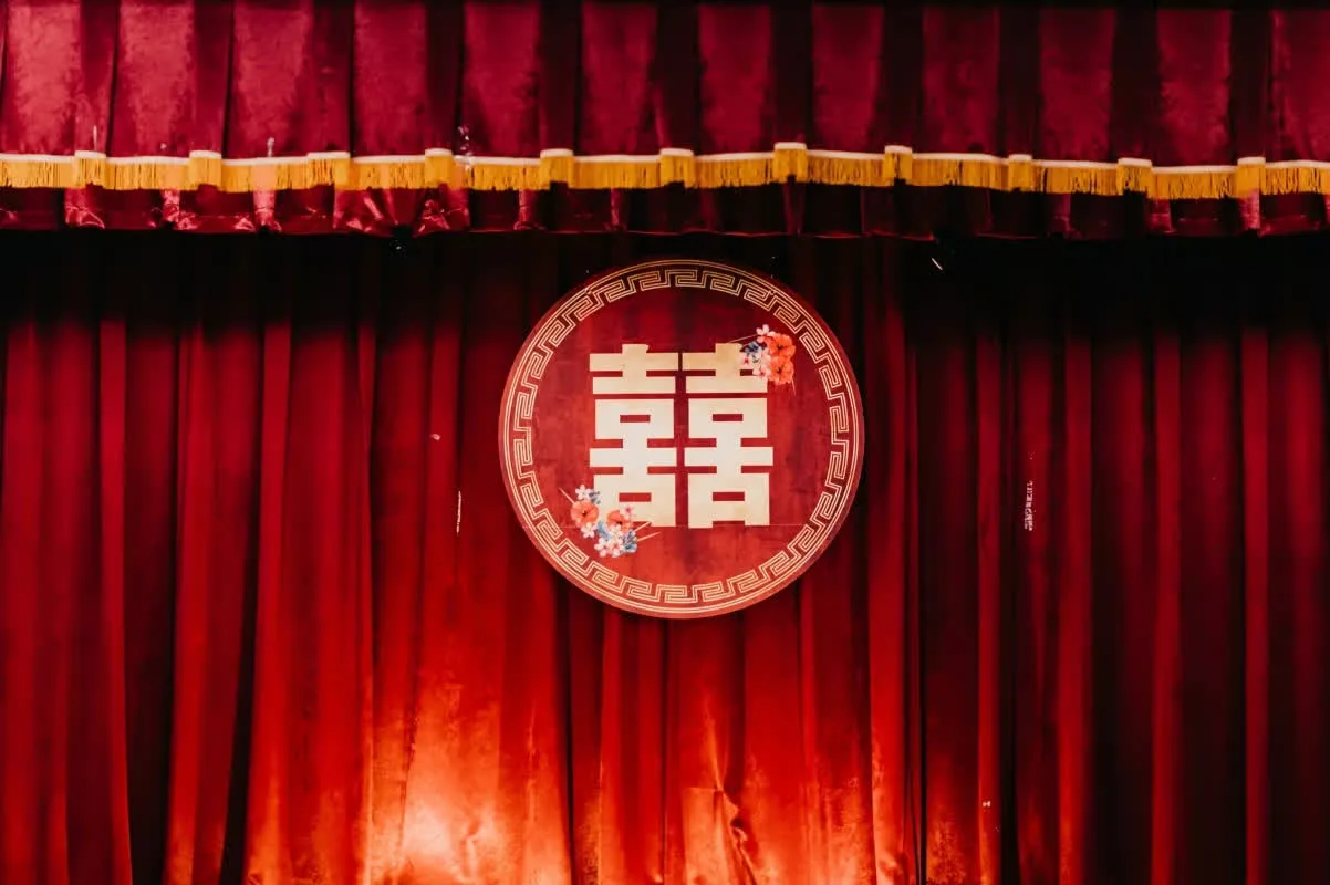 紅色舞台絨布背景，中央圓形囍字牌匾點綴花卉，營造喜慶婚禮氛圍。
