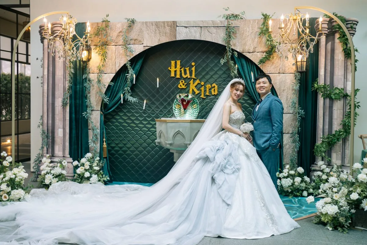 新婚夫婦立於綠色古樸拱門前，綴滿白花與金色飾品，神祕蛇形裝飾獨特雅緻。