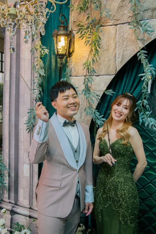 新婚夫婦在綠意盎然、魔幻風格的婚禮場景中,手持魔杖開心地笑著
