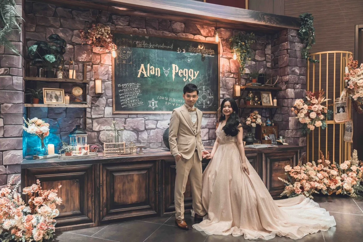 穿著禮服的新婚夫婦,站在魔幻實驗室主題的石牆前,周圍有溫暖色調的花藝裝飾。