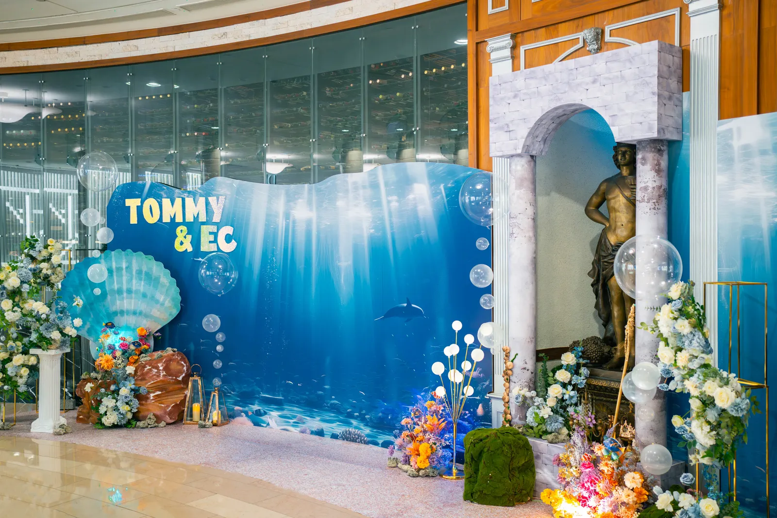 海洋主題婚禮現場全景，海洋透光背板、貝殼花藝與代理海神雕像一字排開